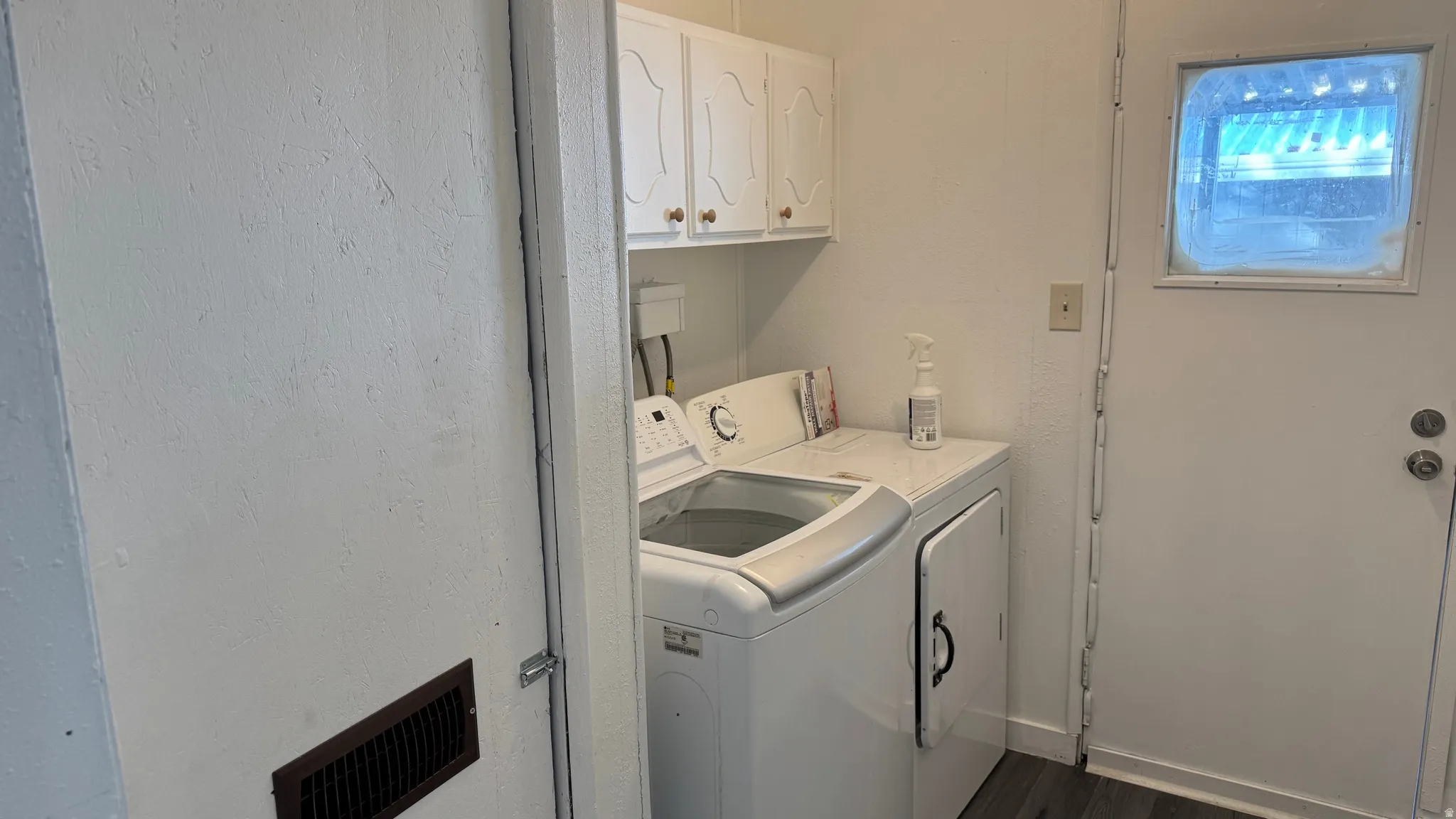 Laundry room featuring cabinet space, washing machine and clothes dryer, dark wood-type flooring, and a textured wall
