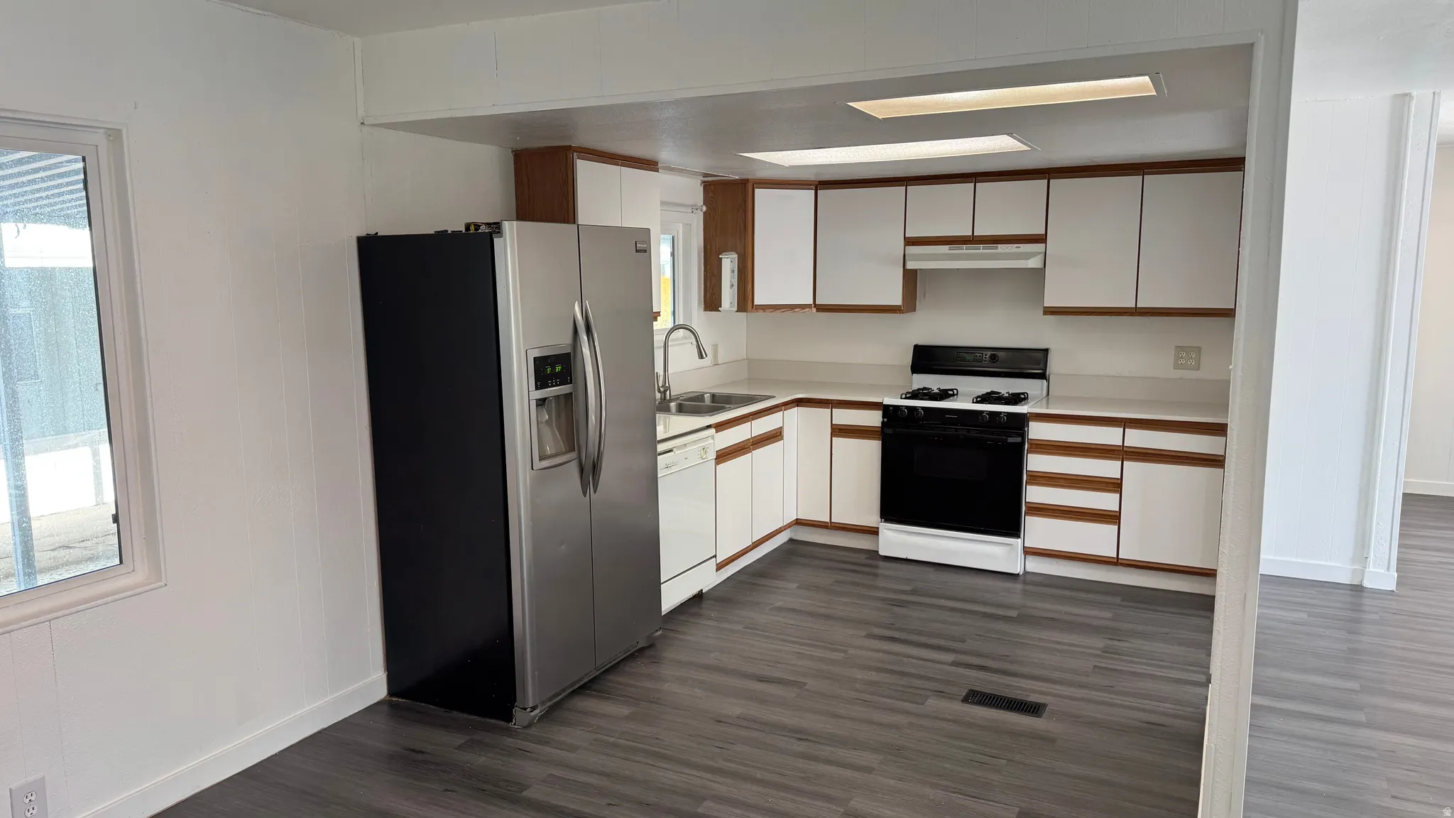 Kitchen with white cabinets, light countertops, stainless steel fridge, gas stove, and dark wood-type flooring