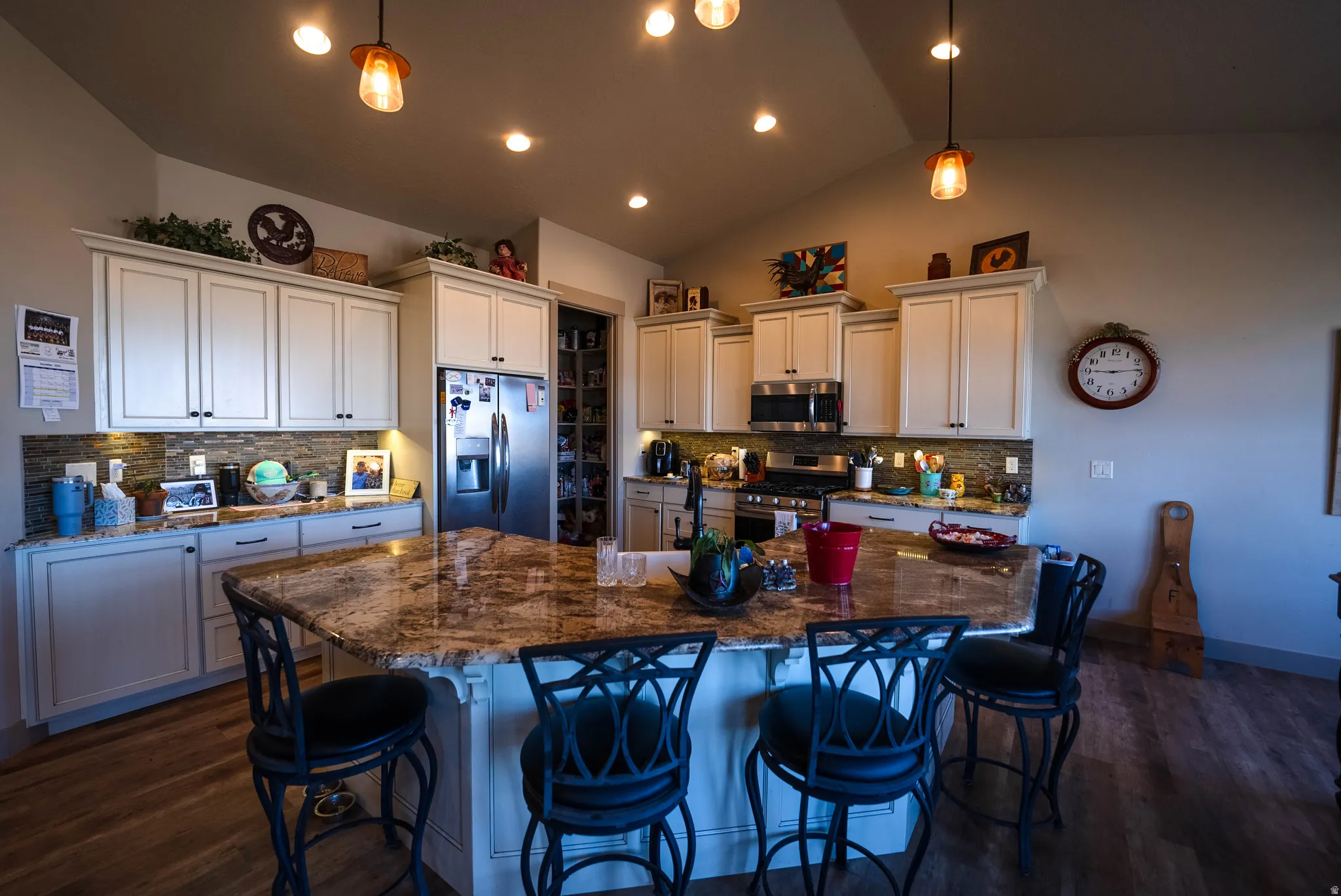 Kitchen with backsplash, stainless steel appliances, pendant lighting, white cabinets, and lofted ceiling