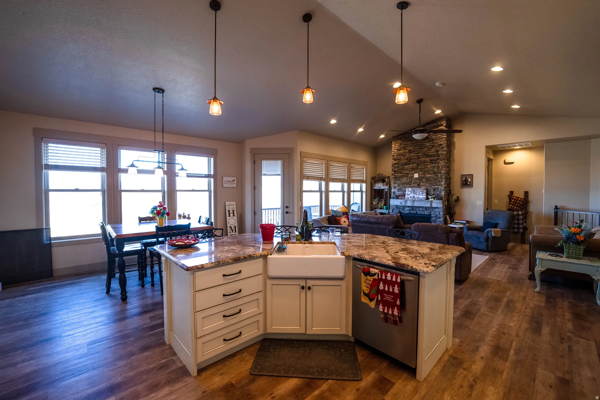 Kitchen with light stone counters, pendant lighting, a center island, stainless steel dishwasher, and dark wood-type flooring
