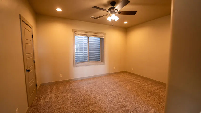 Carpeted room featuring a ceiling fan with integrated lighting, recessed lighting, and a three-panel interior door with black hardware