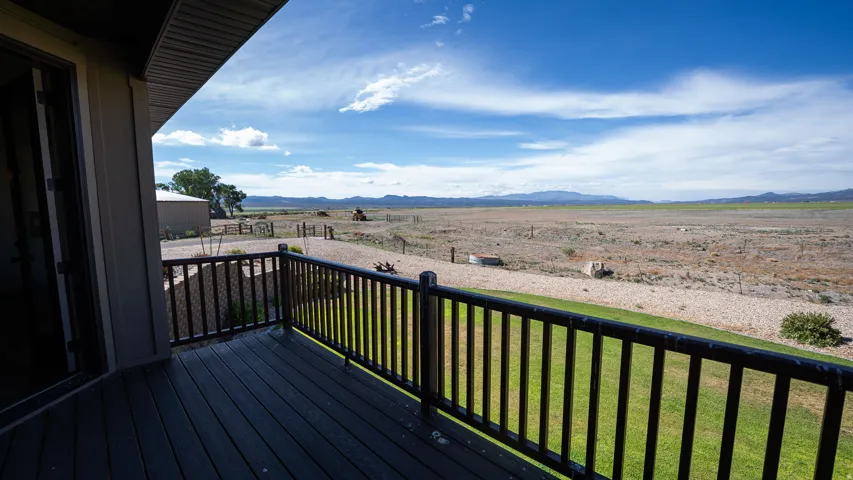 Expansive outdoor deck with dark wood-finish flooring and a black spindle railing, featuring a wide vista of distant mountains and open terrain