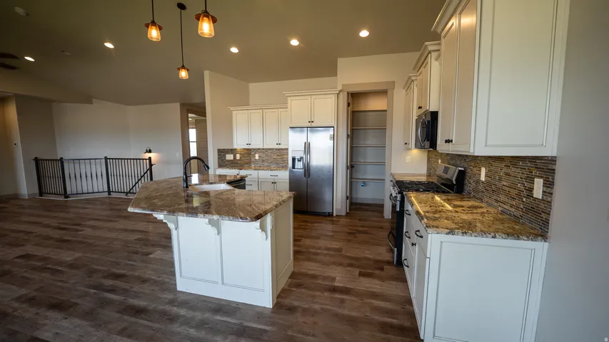 Kitchen featuring a central island with an undermount sink, granite countertops, wood-finish flooring, white cabinetry, stainless steel appliances, and a tiled backsplash