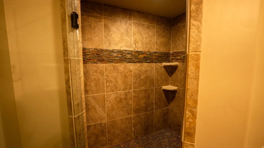 Tile shower enclosure featuring a decorative mosaic accent band and two built-in corner shelves
