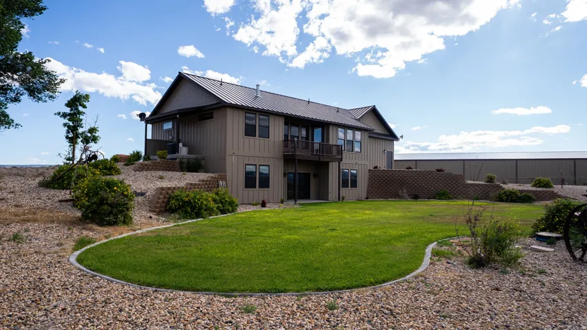 Rear exterior featuring a tiered retaining wall, a metal roof, a second-story balcony, and a lower patio