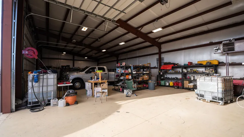 Spacious metal building featuring a large overhead door, concrete flooring, exposed metal beam structure, and integrated fluorescent lighting