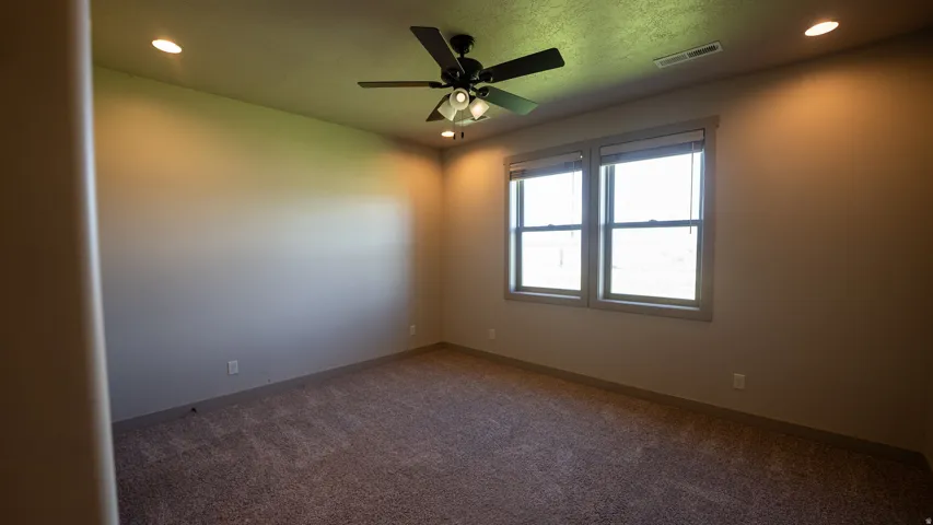 Carpeted interior space featuring two windows with blinds, a ceiling fan with integrated lighting, and recessed ceiling lights