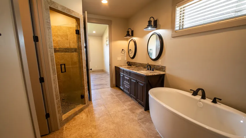 Bathroom featuring a freestanding tub with matte black fixtures, a dual vanity with a stone countertop, a tiled walk-in shower with a glass enclosure, and tiled flooring