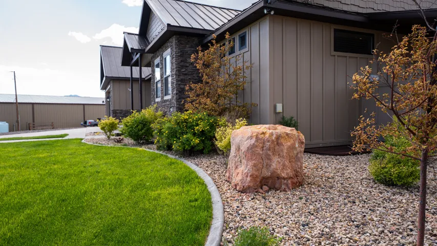 Front exterior featuring a metal roof, stone accents, board and batten siding, and a landscaped gravel bed with a large boulder