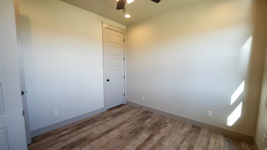 Room featuring wood-finish flooring, light gray walls, a five-panel interior door with black hardware, and recessed lighting
