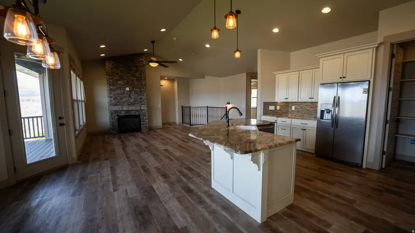 Open-concept living space featuring wood-finish flooring, a stone-clad fireplace, and a kitchen island with a granite-style countertop