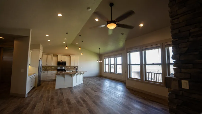 Open-concept living space featuring wood-finish flooring, a vaulted ceiling, and a stone-clad column
