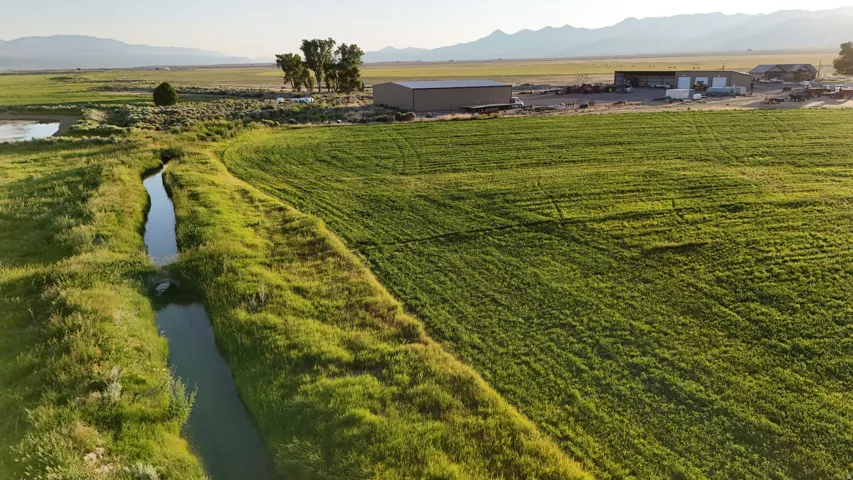 Expansive agricultural land featuring a verdant field, irrigation canal, and distant mountains