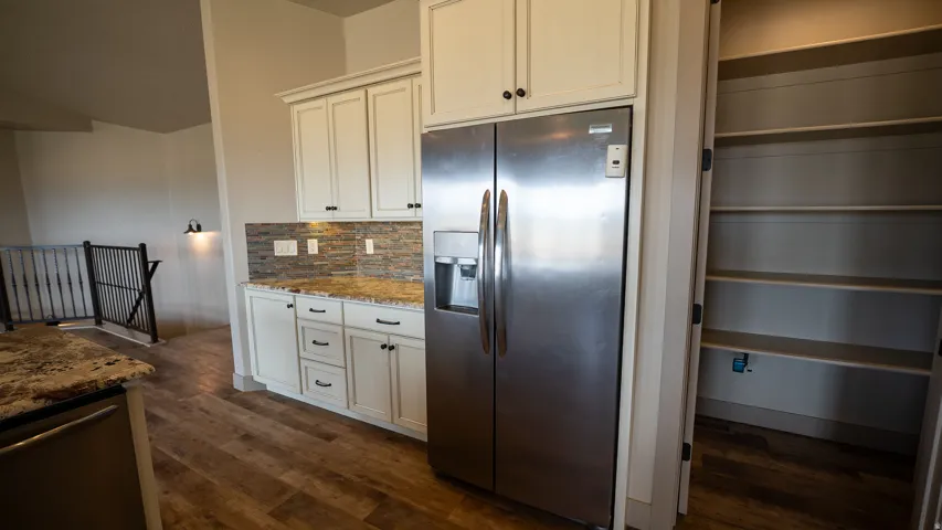 Kitchen featuring wood-finish flooring, white cabinetry, granite-style countertops, a mosaic tile backsplash, and a stainless steel side-by-side refrigerator with dispenser