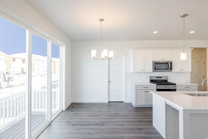 Kitchen featuring stainless steel appliances, white cabinets, dark wood-style flooring, suspended lighting, and light stone counters