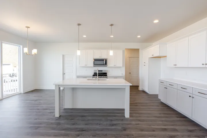 Kitchen featuring white cabinets, dark wood-style floors, stainless steel appliances, suspended lighting, and a kitchen island with sink