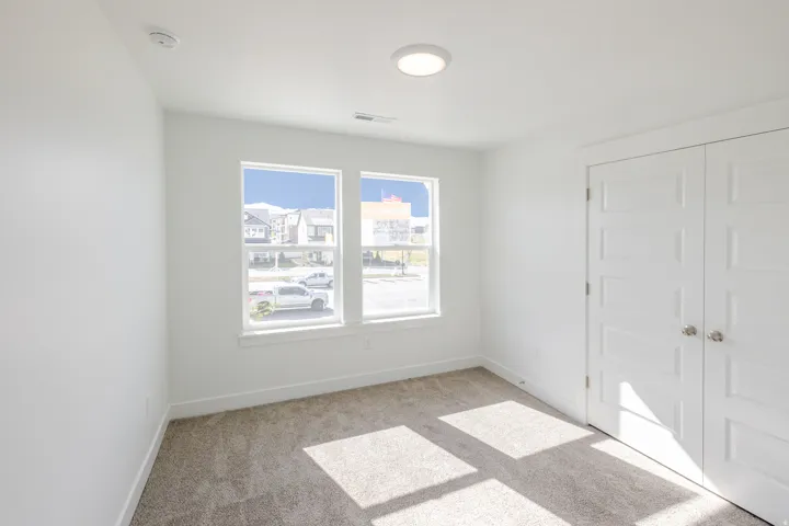 Empty room with light colored carpet and a smoke detector