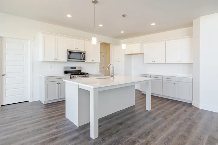 Kitchen featuring white cabinets, stainless steel appliances, dark wood-style flooring, a center island with sink, and hanging light fixtures