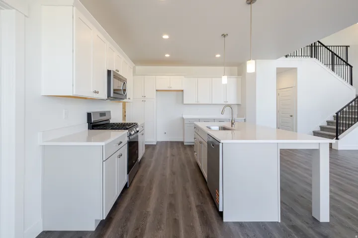 Kitchen with white cabinets, stainless steel appliances, a center island with sink, dark wood finished floors, and hanging light fixtures