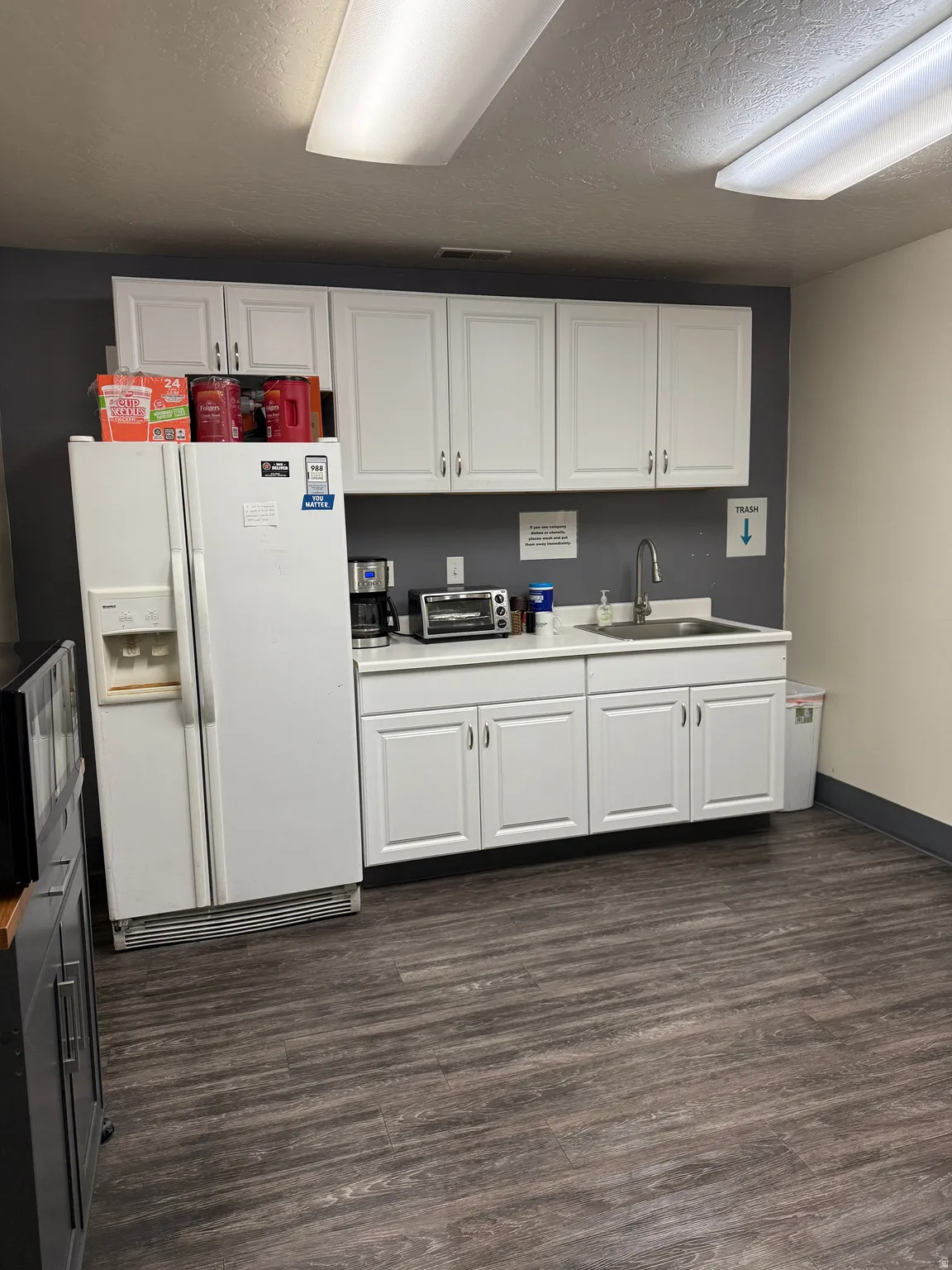 Kitchen with white fridge with ice dispenser, white cabinets, light countertops, dark wood-style flooring, and a textured ceiling