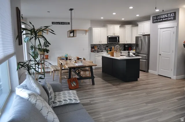 Kitchen featuring white cabinets, stainless steel appliances, light countertops, a center island with sink, and recessed lighting