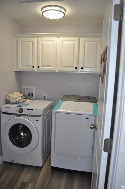 Washroom with cabinet space, washing machine and dryer, dark wood-style flooring, and a textured ceiling
