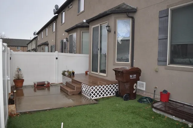 View of side of home featuring a fenced backyard, stucco siding, a wooden deck, and a patio