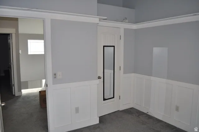 Empty room featuring a wainscoted wall, a decorative wall, and dark colored carpet
