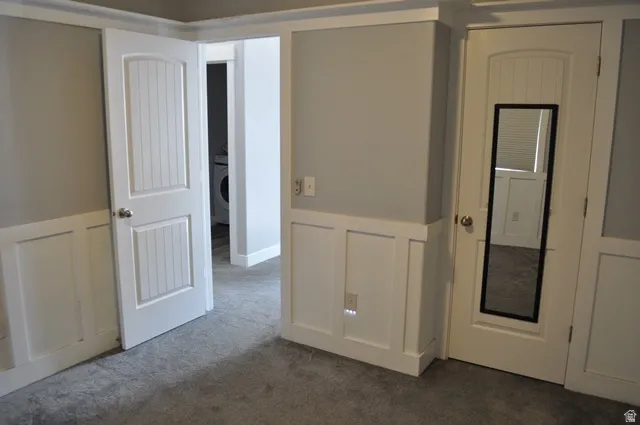 Unfurnished bedroom with a decorative wall, a wainscoted wall, carpet, and washer / dryer