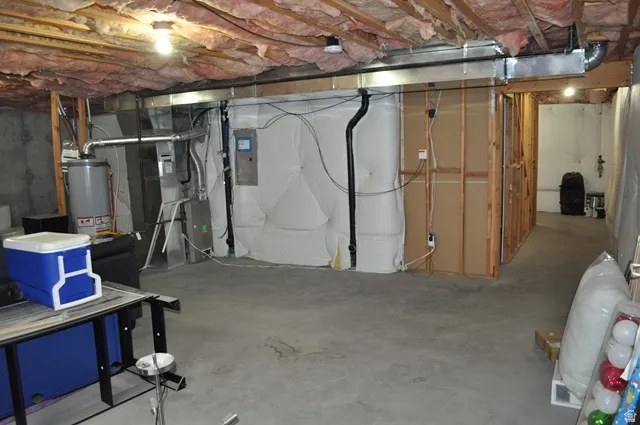 Unfinished basement with electric panel, gas water heater, and heating unit