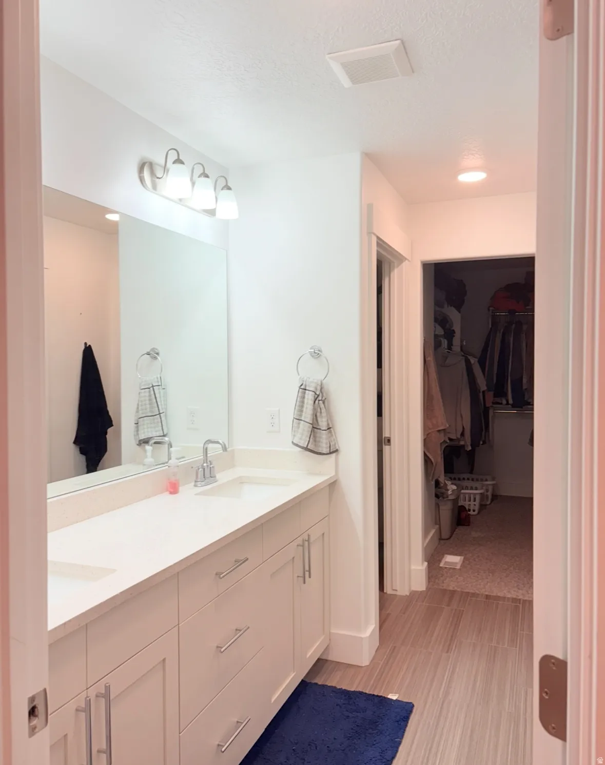 Full bath featuring a walk in closet, double vanity, light wood-style flooring, and a textured ceiling