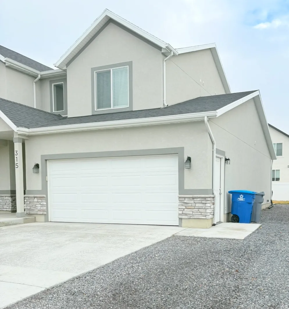 View of side of property featuring stone siding, stucco siding, concrete driveway, and a garage