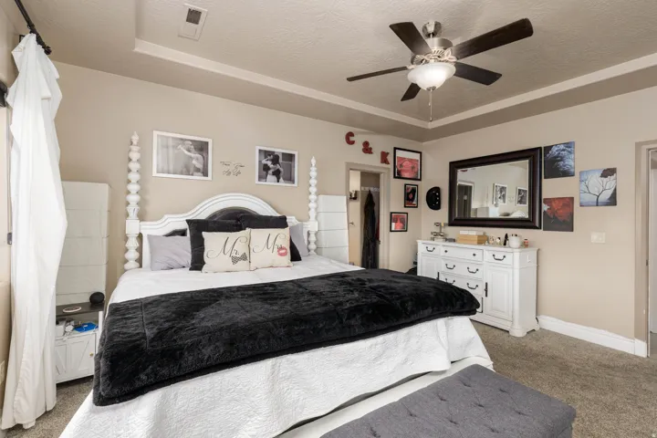 Bedroom featuring light carpet, a raised ceiling, a textured ceiling, and a ceiling fan