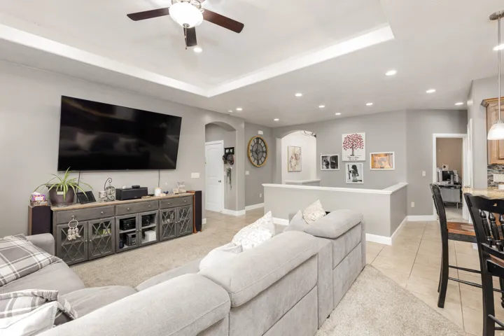 Living area with arched walkways, a raised ceiling, light tile patterned floors, recessed lighting, and ceiling fan