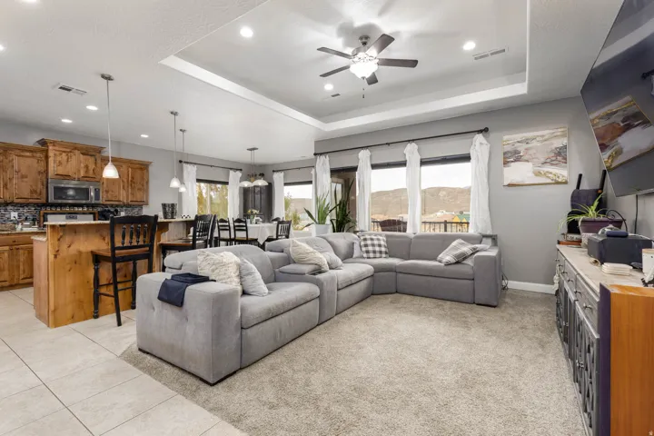 Living room with a tray ceiling, ceiling fan, recessed lighting, and light tile patterned floors