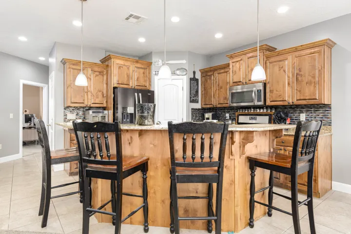 Kitchen with decorative backsplash, a breakfast bar area, stainless steel appliances, light tile patterned floors, and pendant lighting