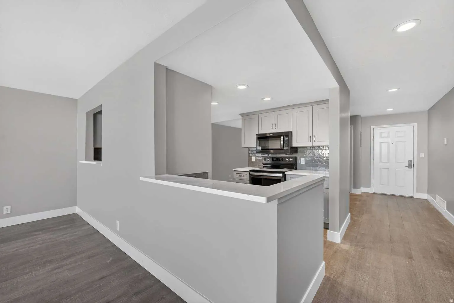 Kitchen with stainless steel electric range oven, black microwave, light wood finished floors, tasteful backsplash, and a peninsula