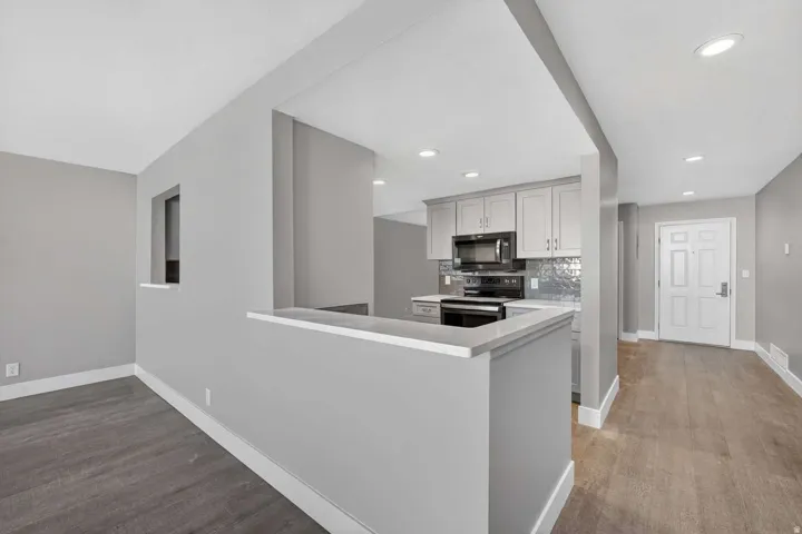 Kitchen with stainless steel electric range oven, black microwave, light wood finished floors, tasteful backsplash, and a peninsula