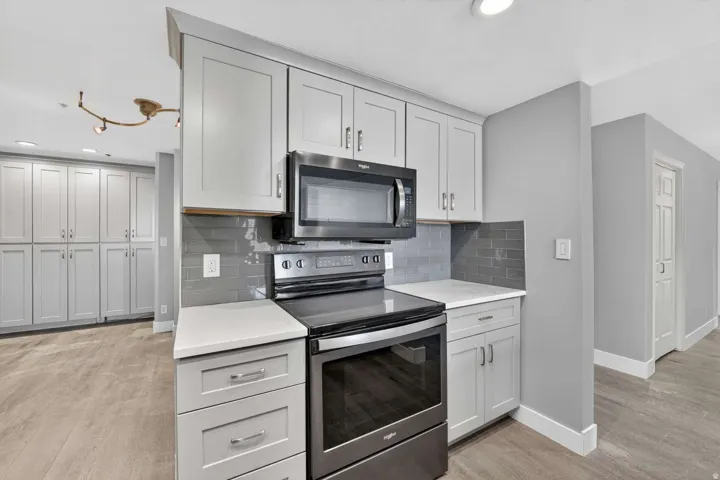 Kitchen featuring electric range, decorative backsplash, light stone counters, light wood finished floors, and recessed lighting