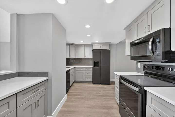 Kitchen featuring black appliances, gray cabinetry, decorative backsplash, light stone counters, and recessed lighting