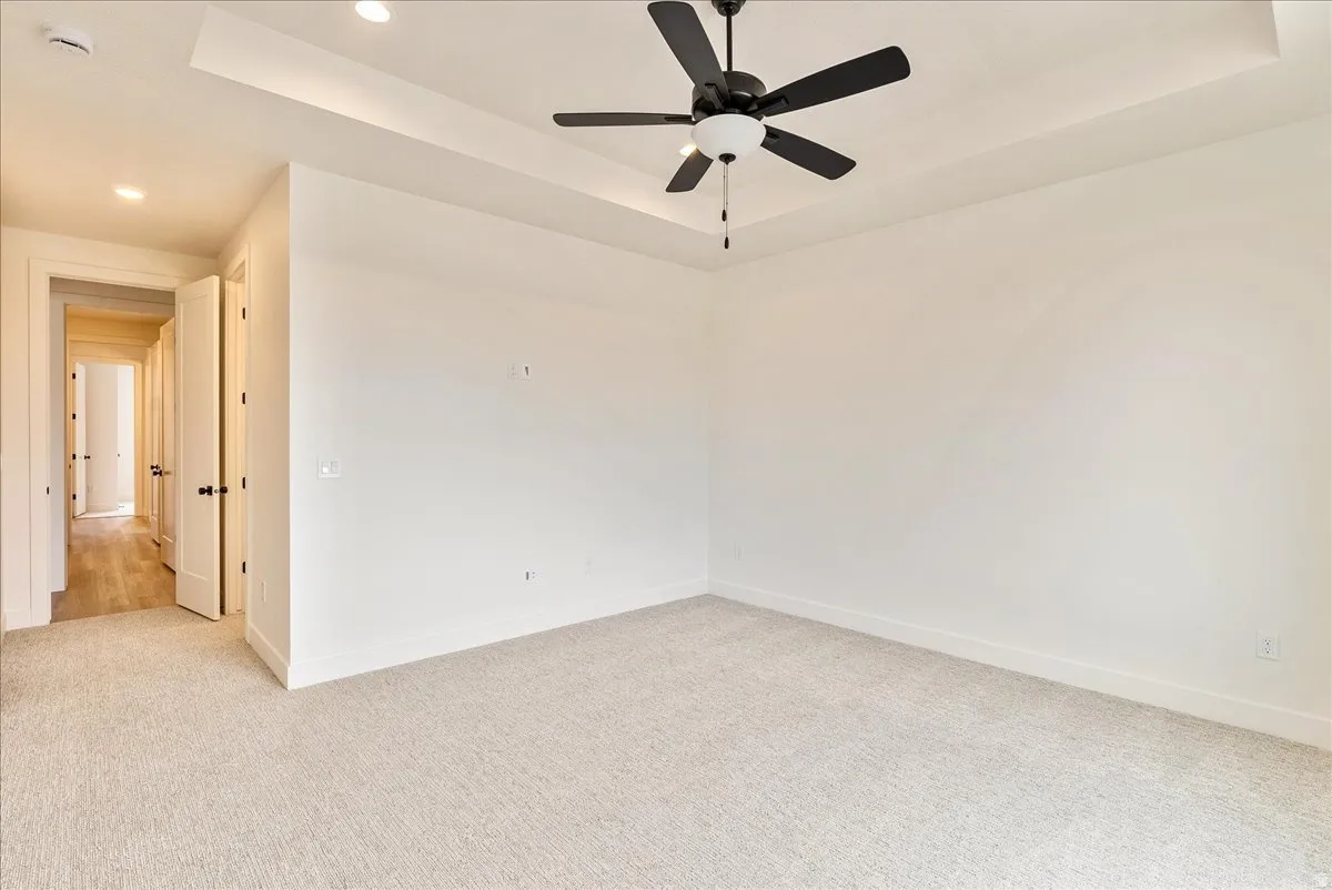 Empty room featuring a raised ceiling, light carpet, a ceiling fan, recessed lighting, and a smoke detector