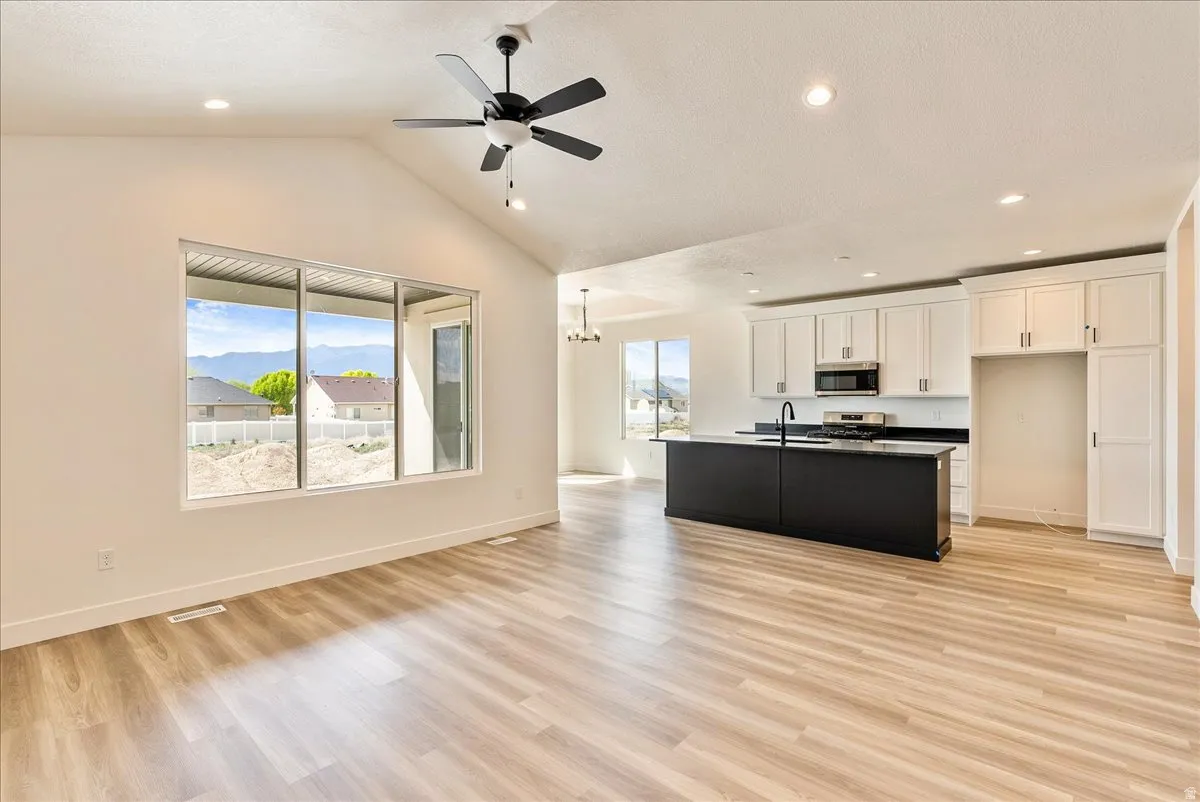 Dual tone kitchen with open floor plan, a ceiling fan, light wood-style floors, stainless steel appliances, and a kitchen island with sink