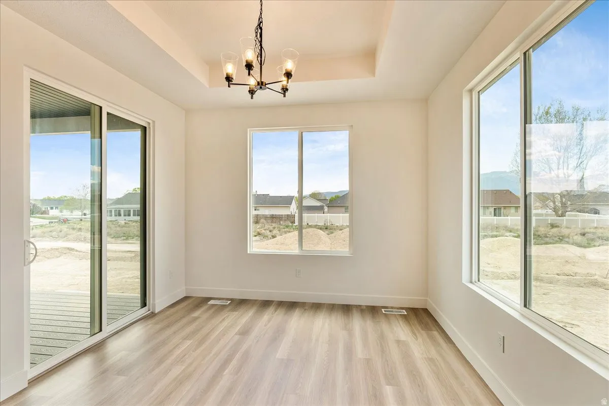 Unfurnished dining area featuring a tray ceiling, suspended lighting, and light wood finished floors
