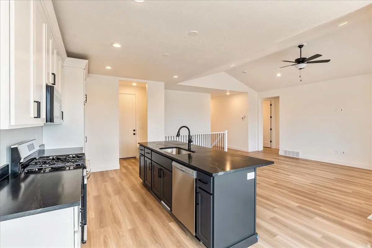 Kitchen with stainless steel appliances, light wood-style flooring, a kitchen island with sink, a ceiling fan, and open floor plan