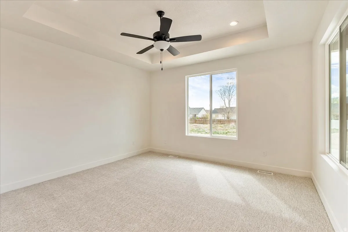 Carpeted empty room with a raised ceiling, a ceiling fan, and recessed lighting