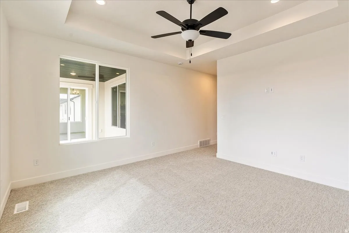 Empty room with a raised ceiling, ceiling fan, carpet, and recessed lighting