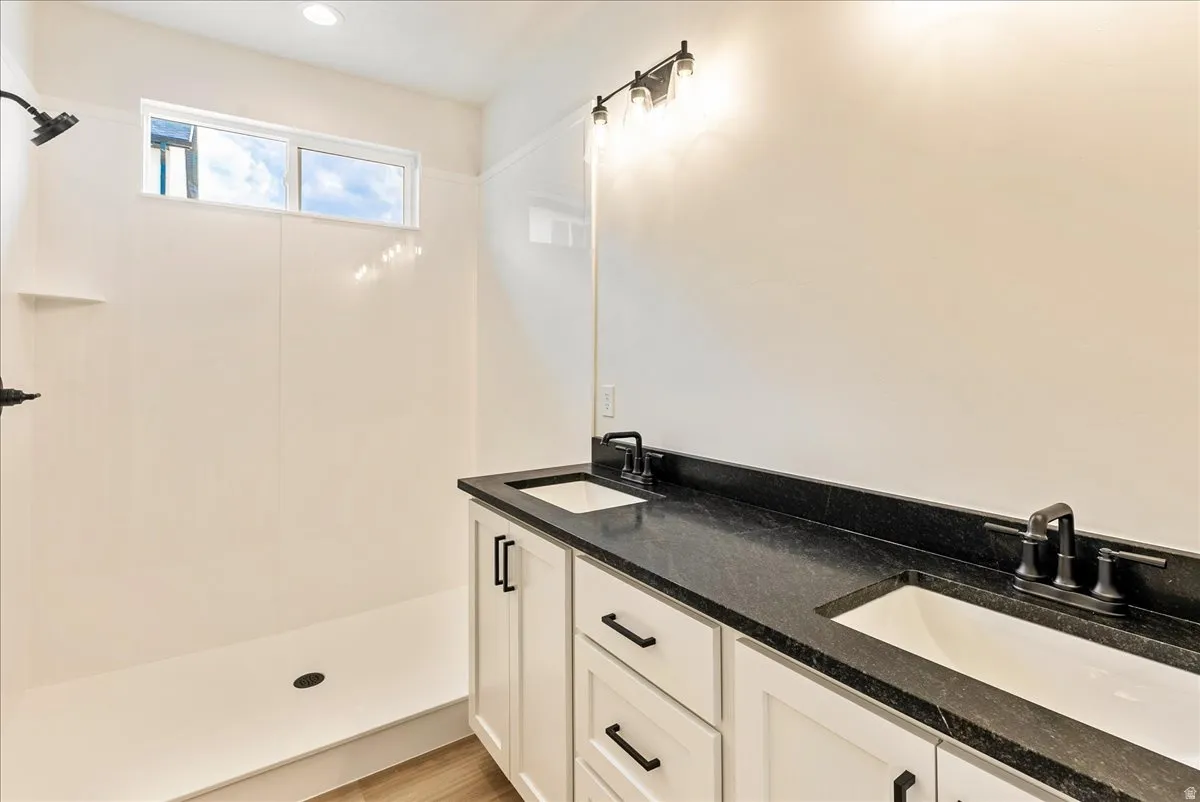 Full bathroom with double vanity, light wood-style flooring, and a walk in shower