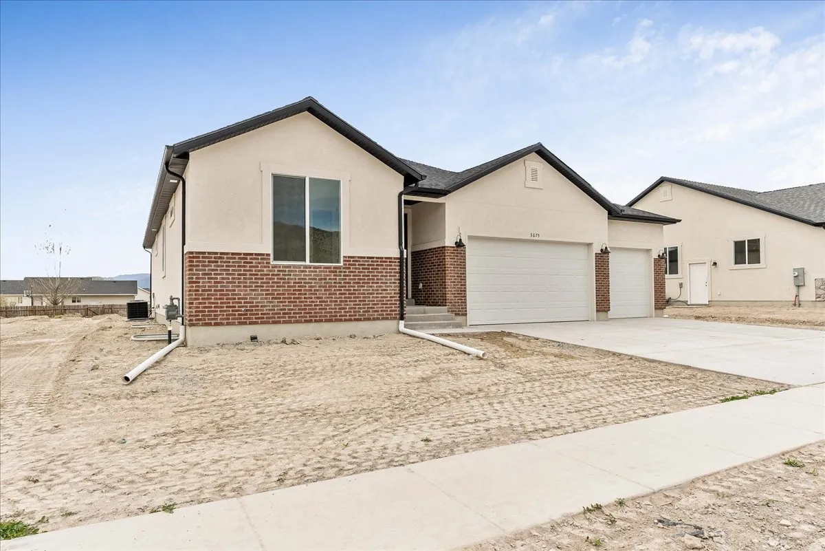 View of front facade with brick siding, a garage, driveway, and stucco siding