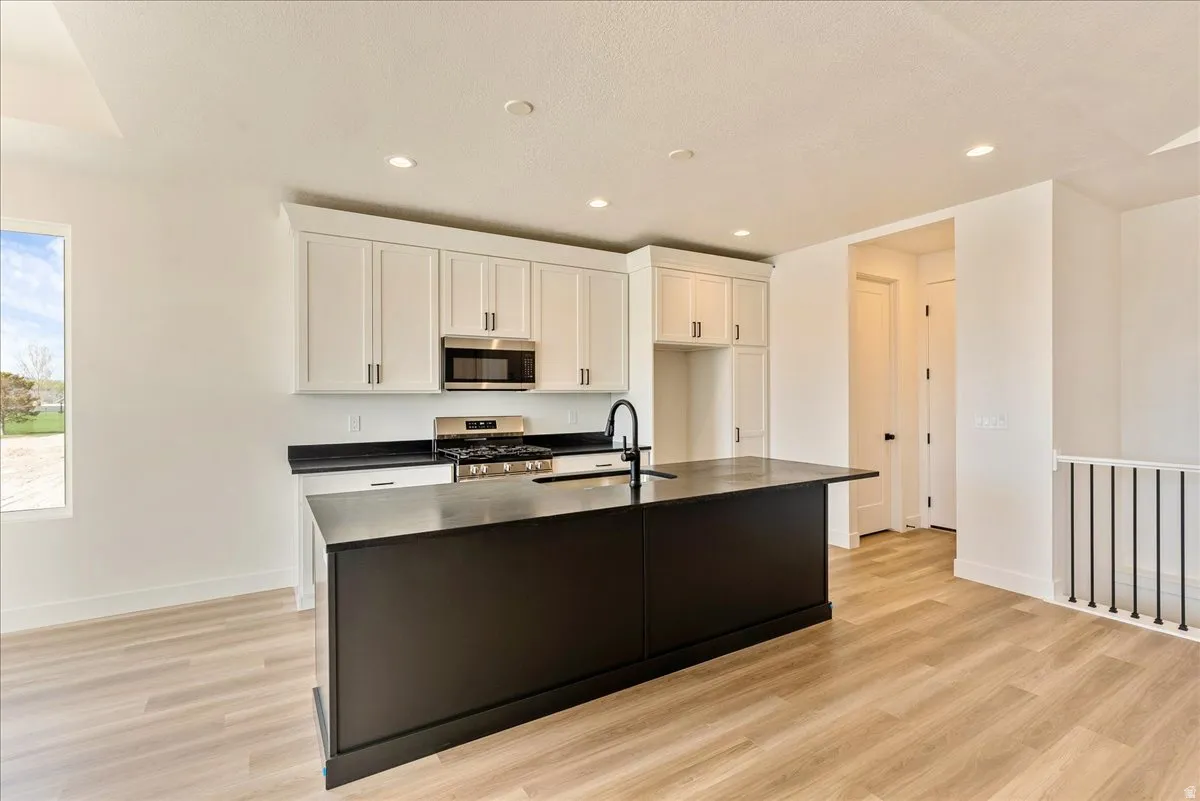 Kitchen with white cabinets, stainless steel appliances, light wood-style floors, a kitchen island with sink, and recessed lighting
