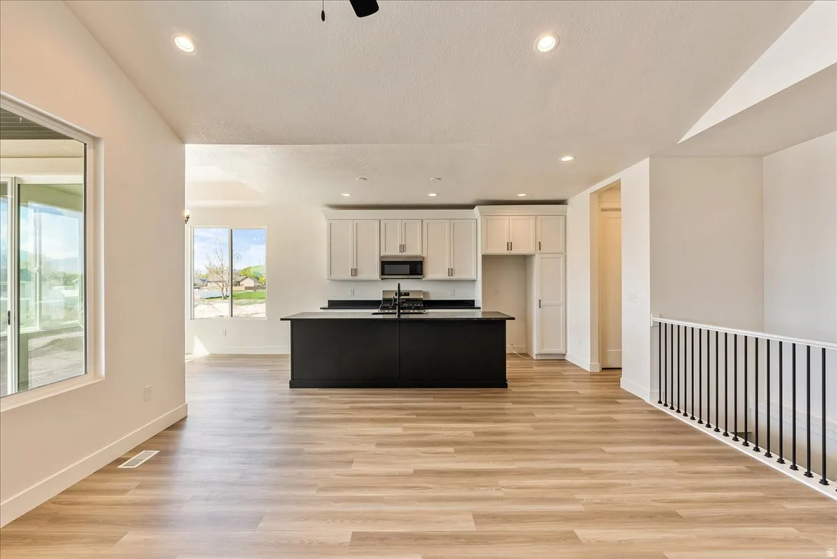Kitchen with light wood-style flooring, a kitchen island with sink, white cabinetry, recessed lighting, and stainless steel microwave